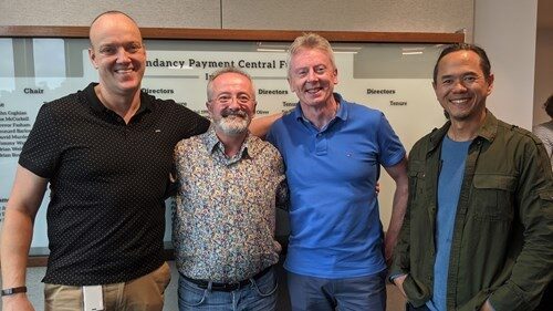 Four people in casual wear standing together and smiling.