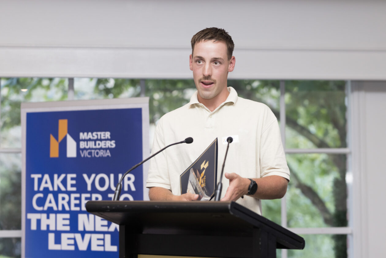 A young apprentice speaking from behind a lectern while holding an award